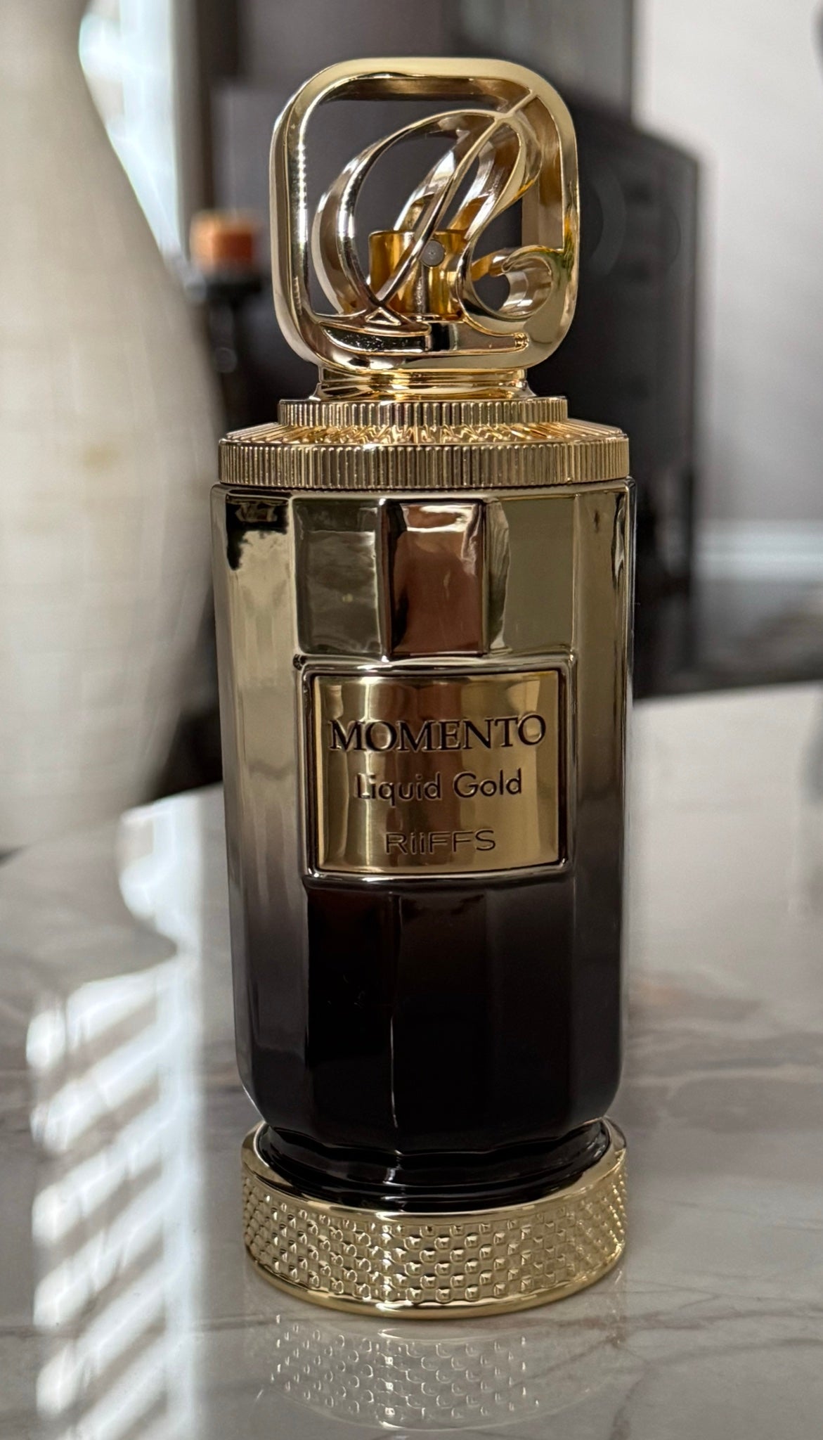 Riiffs Momento Liquid Gold perfume bottle with gold cap on a marble table